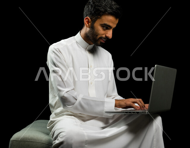 رجل عربي سعودي خليجي يرتدي الزي السعودي، إستخدام جهاز اللابتوب لإنجاز المهام، التسوق الإلكتروني، تطور التكنولوجيا وإستخدام الأجهزة التقنية الحديثة، إجتماع عمل، إدارة الأعمال عن بعد، تصفح الانترنت, إجراء مكالمات فيديو عبر جهاز الحاسوب, خلفيه سوداء
