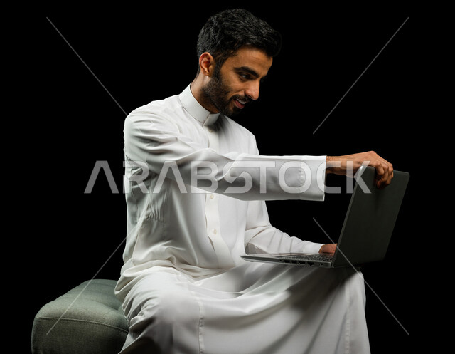 رجل عربي سعودي خليجي يرتدي الزي السعودي، إستخدام جهاز اللابتوب لإنجاز المهام، التسوق الإلكتروني، تطور التكنولوجيا وإستخدام الأجهزة التقنية الحديثة، إجتماع عمل، إدارة الأعمال عن بعد، تصفح الانترنت, إجراء مكالمات فيديو عبر جهاز الحاسوب, خلفيه سوداء