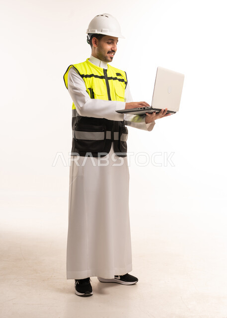 مهندس سعودي يرتدي سترة سلامة ويستخدم لابتوب
