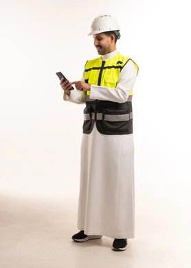 مهندس سعودي يرتدي معدات السلامة ويستخدم الهاتف الذكي