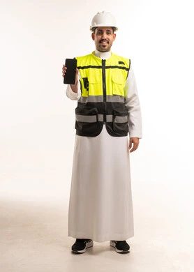 مهندس سعودي يرتدي سترة السلامة ويمسك بهاتف ذكي