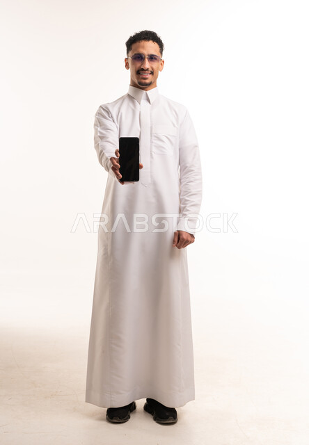 رجل سعودي بالثوب الأبيض يمسك هاتف ذكي في استوديو