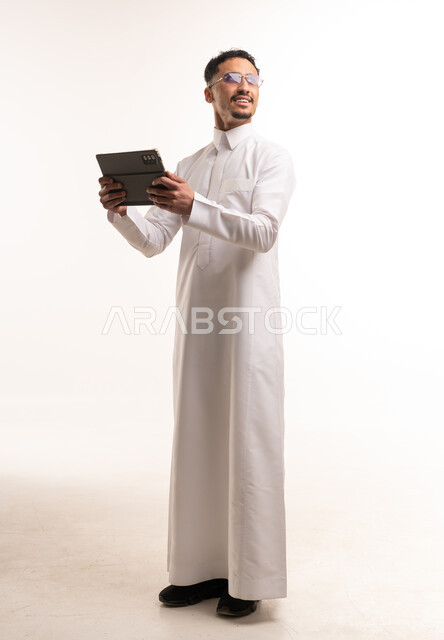 رجل سعودي بالثوب الأبيض يمسك بجهاز لوحي رقمي