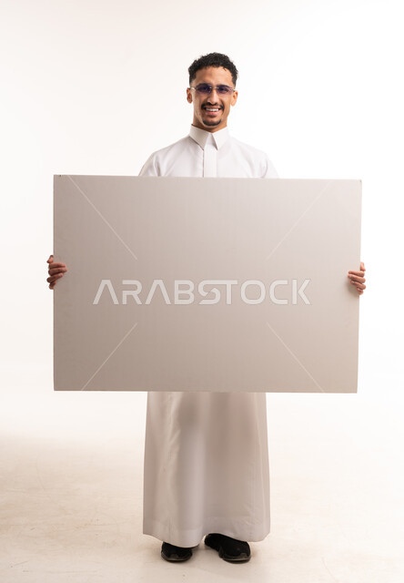 رجل سعودي يحمل لوحة بيضاء فارغة كبيرة في الاستوديو