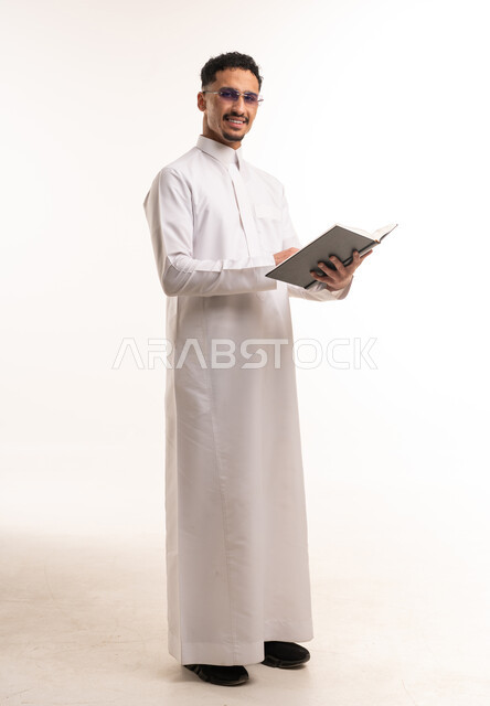 رجل سعودي بالثوب التقليدي يحمل كتاباً في الاستوديو