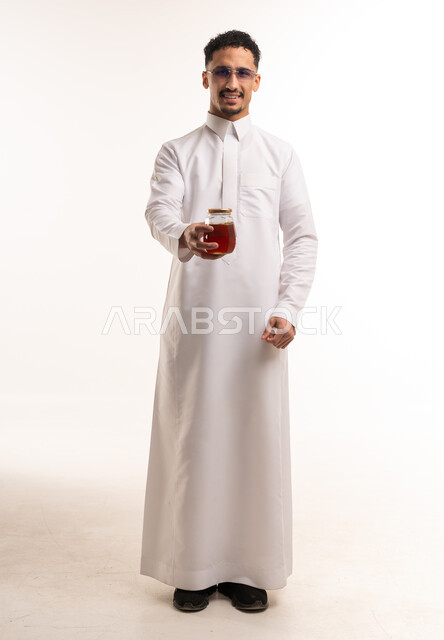 رجل سعودي بالثوب التقليدي يحمل جرة عسل