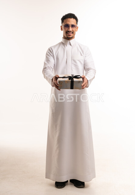 رجل سعودي يرتدي الثوب التقليدي يحمل صندوق هدايا أبيض