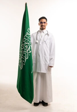 طبيب سعودي بالمعطف الطبي يحمل علم المملكة العربية السعودية