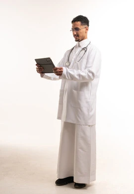 طبيب سعودي يرتدي معطفاً طبياً ويستخدم جهازاً لوحياً