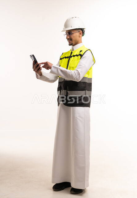 Saudi Engineer in Thobe Using Smartphone with Safety Gear
