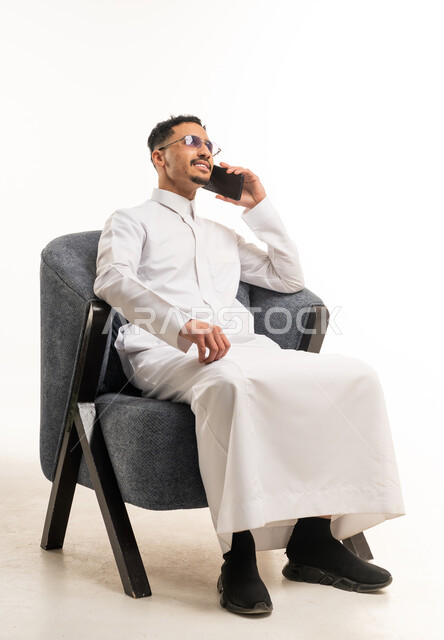 رجل سعودي بالثوب الأبيض يتحدث بالهاتف على كرسي عصري