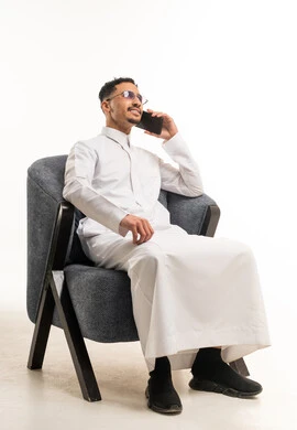 Saudi Man in White Thobe Talking on Phone in Chair