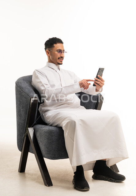 Saudi Man in White Thobe Using Smartphone