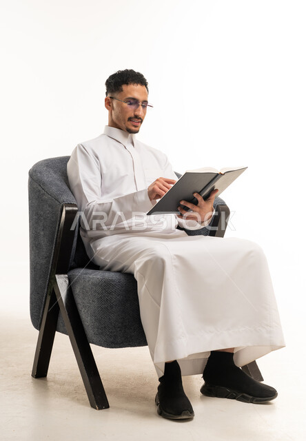 رجل سعودي يقرأ كتاباً على كرسي في استوديو