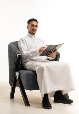 رجل سعودي بالثوب الأبيض يقرأ كتاباً في الاستوديو