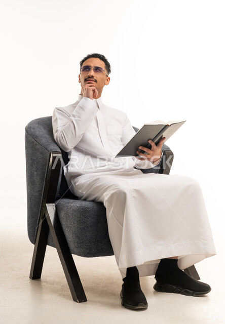 رجل سعودي بالثوب الأبيض يقرأ كتاباً في الاستوديو