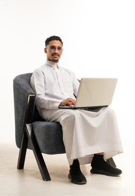 Saudi Man in White Thobe Using Laptop on Armchair