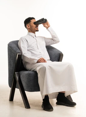 رجل سعودي بالثوب التقليدي يستخدم المنظار في الاستوديو