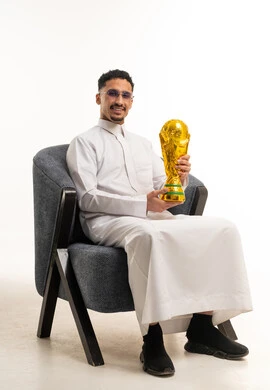 رجل سعودي بالثوب التقليدي يحمل كأس بطولة كرة القدم