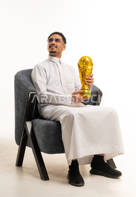 رجل سعودي بالثوب التقليدي يحمل كأساً ذهبياً في الاستوديو