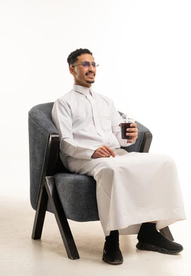 رجل سعودي بالثوب الأبيض يجلس مع مشروب بارد