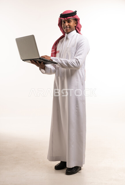 رجل سعودي بالزي التقليدي يحمل جهاز كمبيوتر محمول