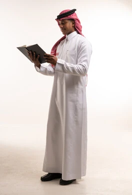 رجل سعودي بالثوب التقليدي يقرأ كتاباً