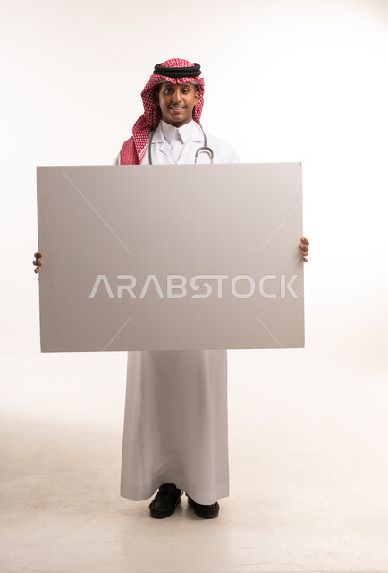 طبيب سعودي يحمل لوحة بيضاء فارغة بخلفية بيضاء