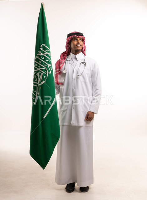 طبيب سعودي يحمل علم المملكة في استوديو أبيض