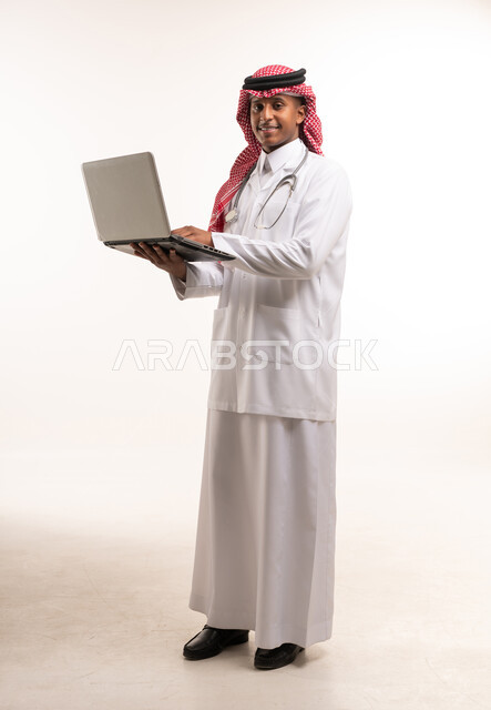 طبيب سعودي يحمل كمبيوتر محمول على خلفية بيضاء