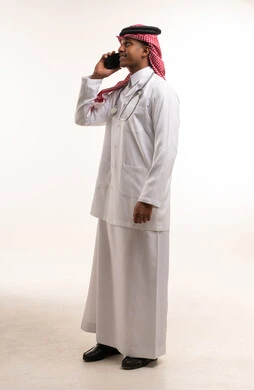 طبيب سعودي يتحدث بالهاتف مرتديًا المعطف الطبي