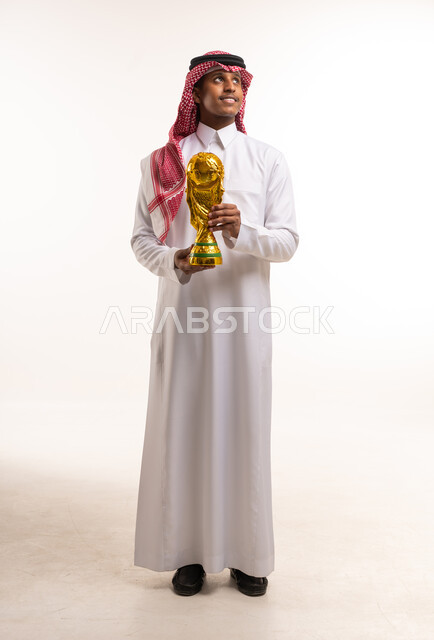 رجل سعودي يحمل مجسم كأس العالم الذهبي في الاستوديو