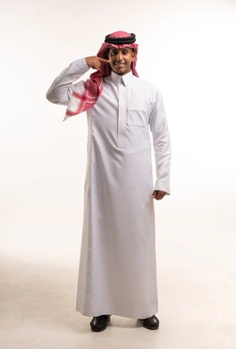 رجل سعودي بالزي التقليدي يشير إلى ابتسامته