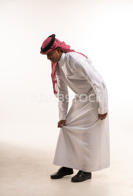 رجل سعودي بالثوب التقليدي يعدل ملابسه في الاستوديو