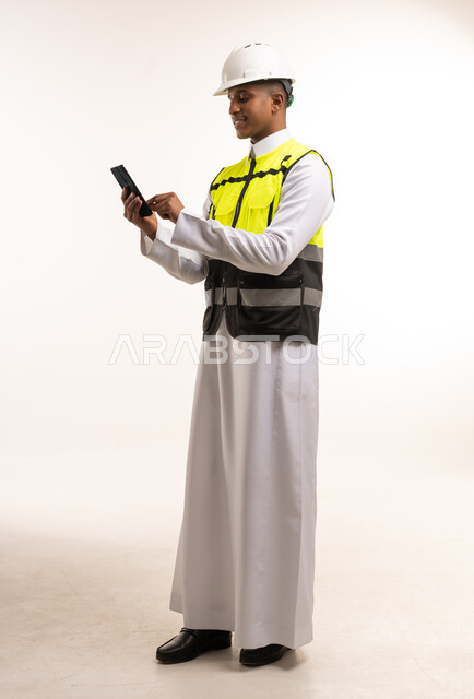 Saudi Engineer in Thobe Using Smartphone with Safety Gear