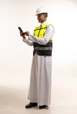 مهندس سعودي بالثوب يستخدم الهاتف مع معدات السلامة