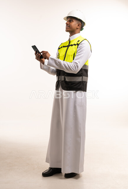 مهندس سعودي يرتدي سترة السلامة ويستخدم الهاتف