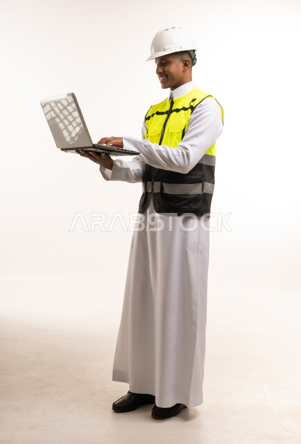 مهندس سعودي يرتدي خوذة ويستخدم حاسوب محمول