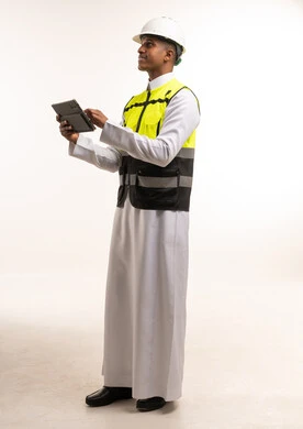 مهندس سعودي بسترة السلامة يستخدم جهاز لوحي بخلفية بيضاء