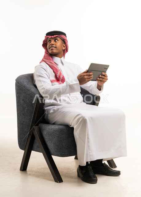 رجل سعودي مع جهاز لوحي يجلس على كرسي في الاستوديو