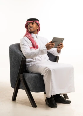 رجل سعودي مع جهاز لوحي يجلس على كرسي في الاستوديو