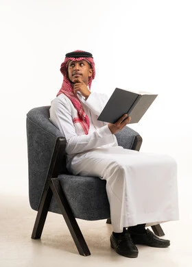 رجل سعودي يقرأ كتاباً على كرسي بخلفية بيضاء