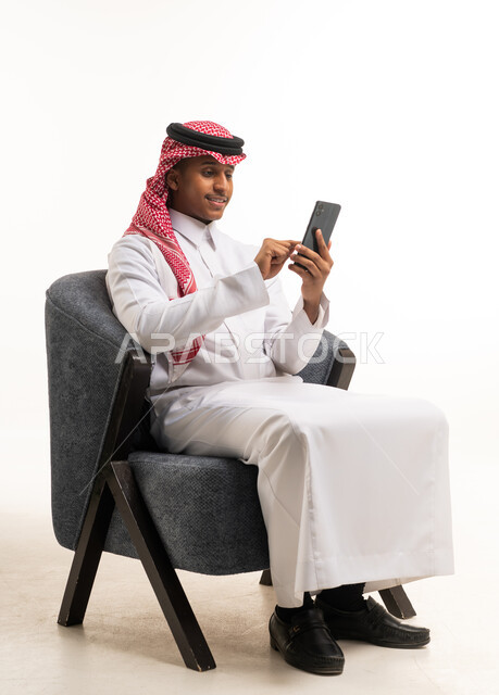 Saudi Man in Thobe Using Smartphone on Armchair