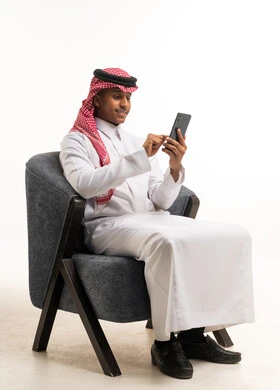 رجل سعودي بالثوب يستخدم الجوال على الكرسي