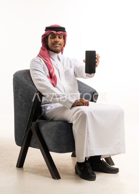 رجل سعودي بالزي التقليدي يحمل هاتفاً ذكياً