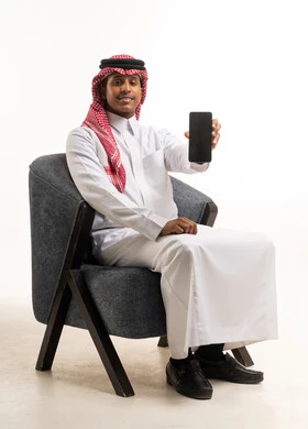 رجل سعودي بالزي التقليدي يحمل هاتفاً ذكياً