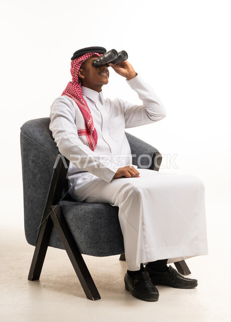 رجل سعودي يستخدم المنظار جالسًا على كرسي استوديو