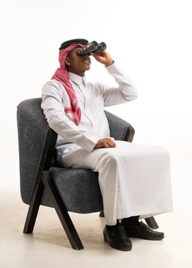 رجل سعودي يستخدم المنظار جالسًا على كرسي استوديو