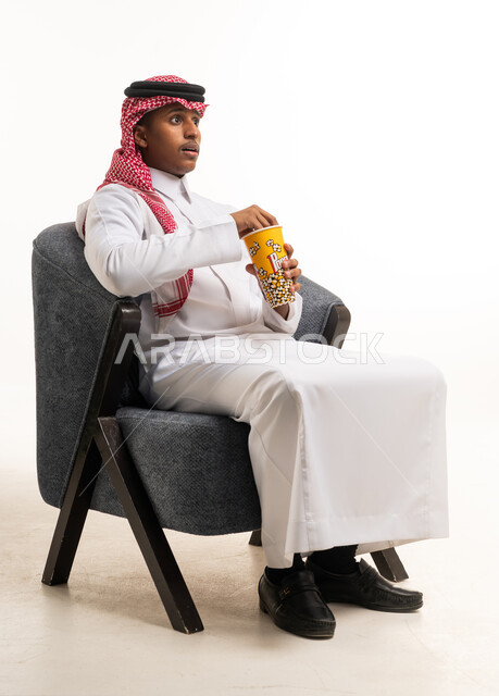 رجل سعودي بالزي التقليدي يشاهد فيلما مع وعاء فشار