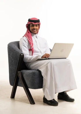 رجل سعودي بالثوب التقليدي يستخدم الكمبيوتر المحمول